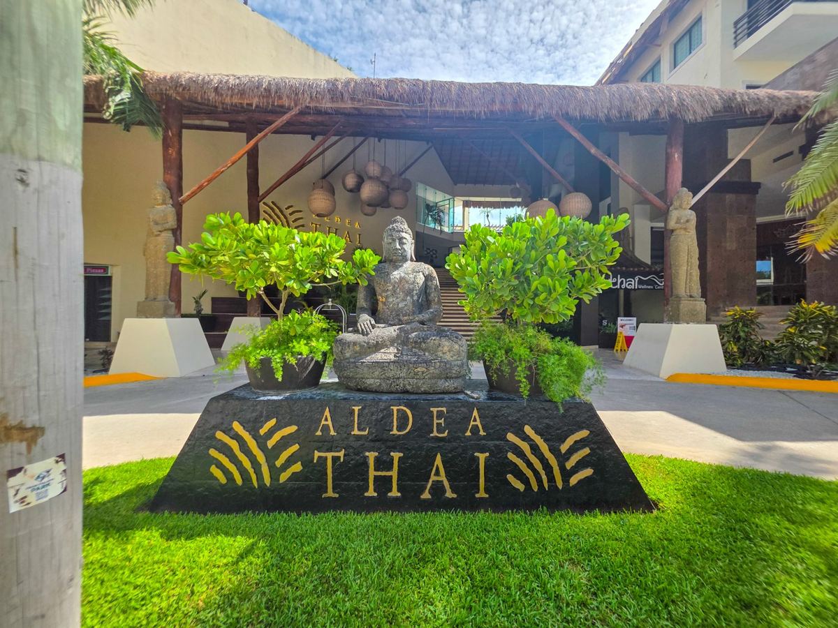 La entrada: un Buda de piedra frente al letrero de Aldea Thai